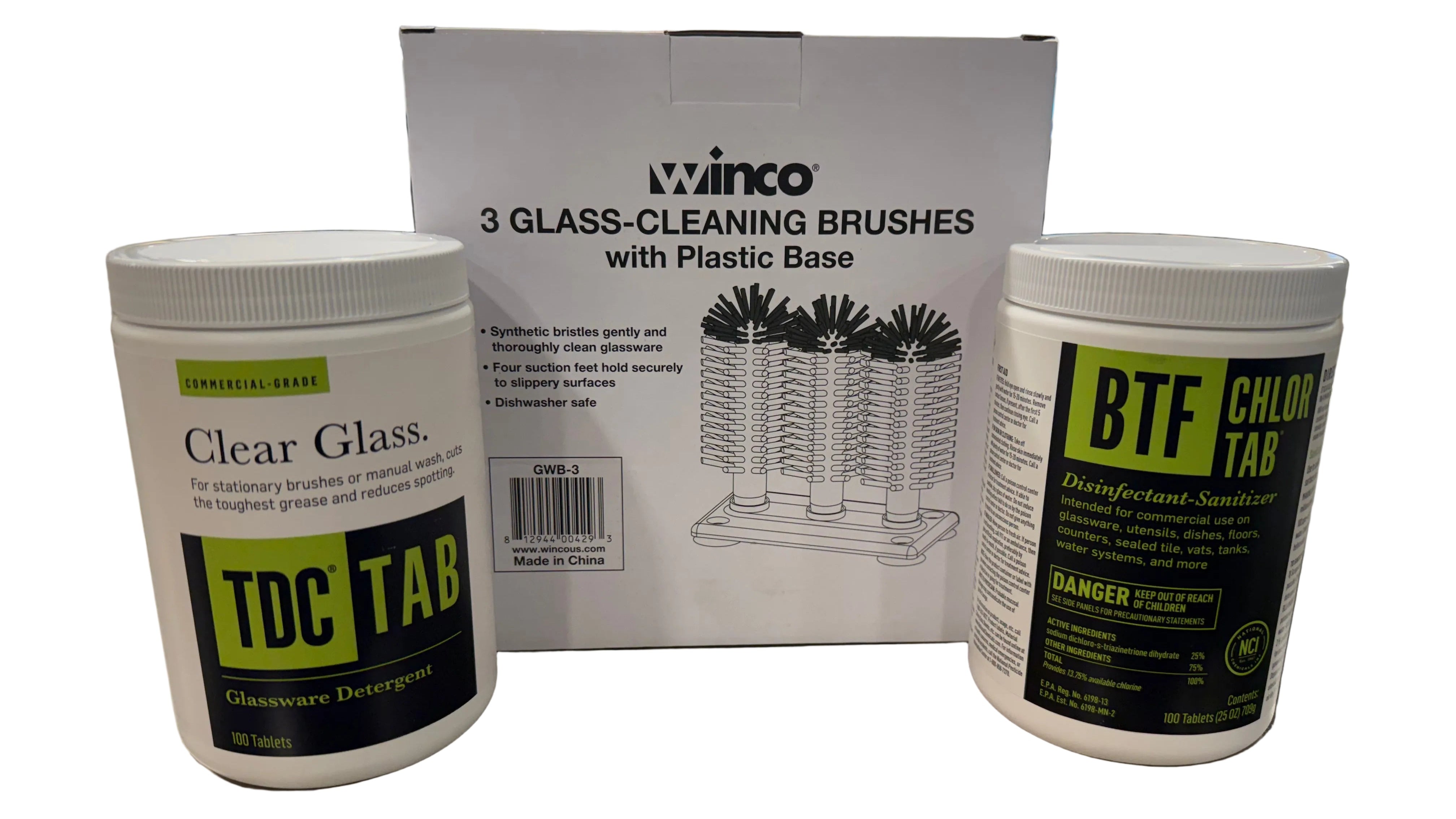A set of Winco glass-cleaning products displayed on a metal counter in a store setting, including a box of 3 glass-cleaning brushes with plastic base, a container of Clear Glass TDC TAB glasswater detergent, and a container of BTF Chlor Tab disinfectant sanitizer.