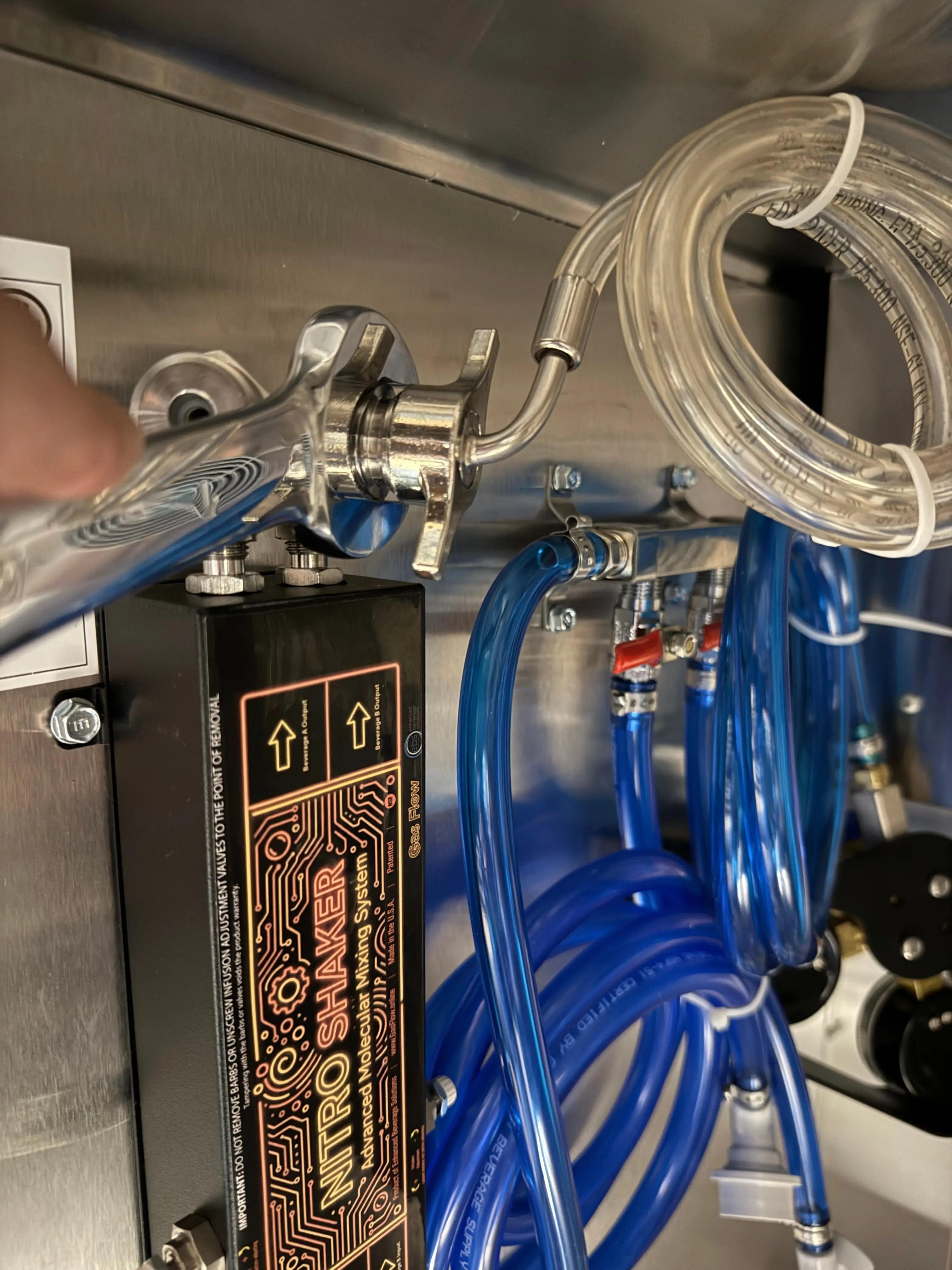 Close-up of a metal valve with hoses and a 'Nitro Shaker' device on a metallic surface.
